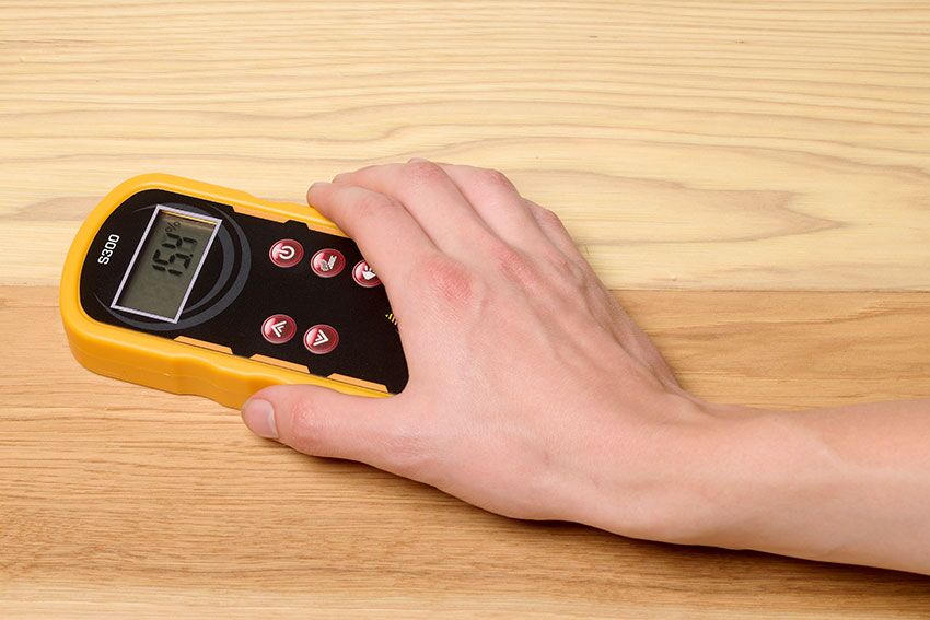 A man's hand holding the S300 Shallow Scan Pinless Wood Moisture Meter on a wood table