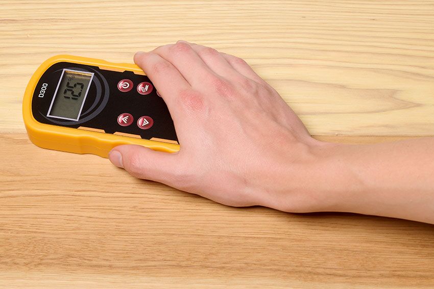 A man's hand holding the D300 Deep Scan Pinless Wood Moisture Meter on a wood table