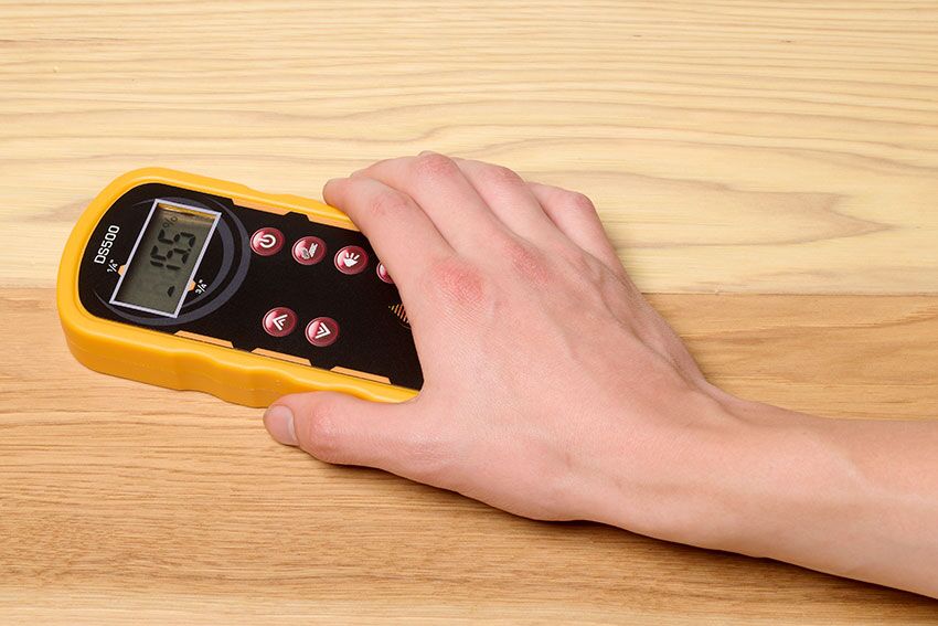 A man's hand holding the DS500 Dual Scan Pinless Wood Moisture Meter on a wood table